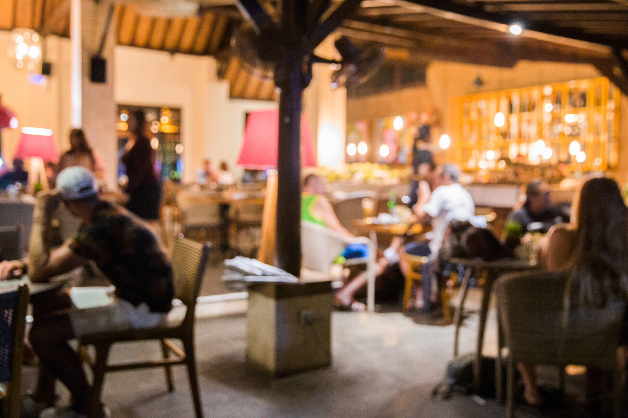 Imagem tem um blur de efeito, mas dá para perceber pessoas sentadas em várias mesas de um bar ou restaurante